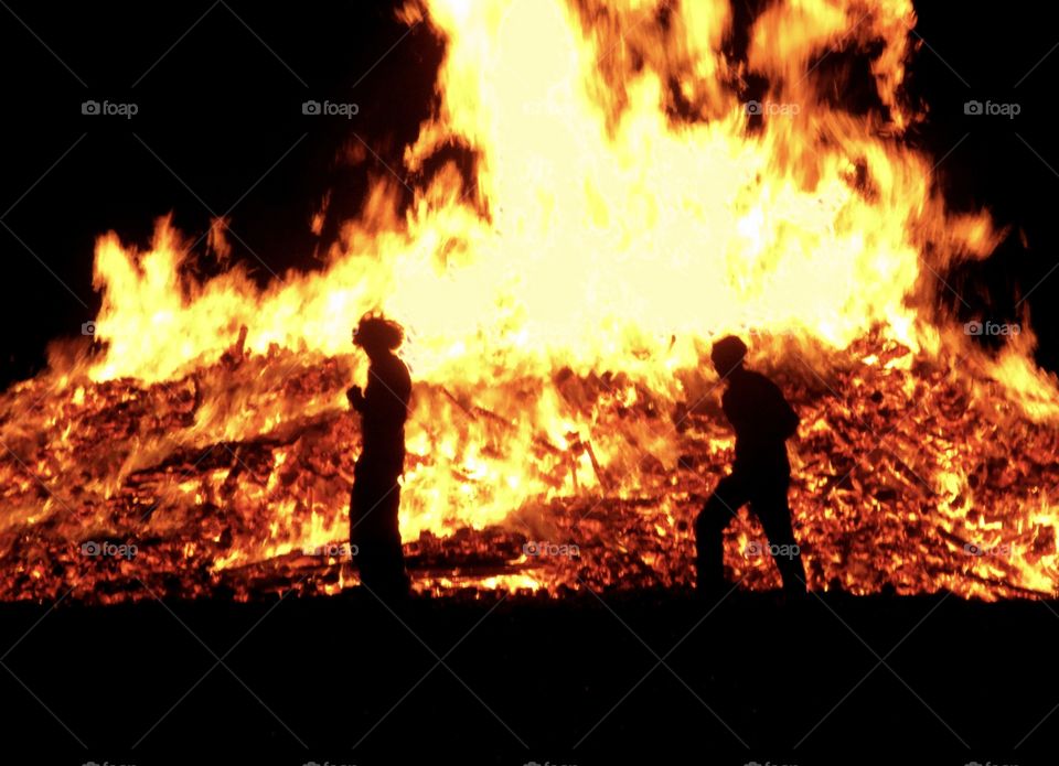 2 people are silhouetted against a roaring bonfire