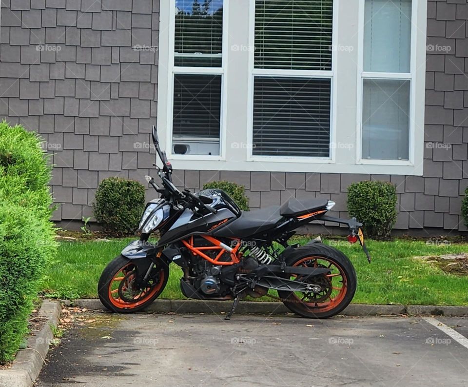 red orange and black motorcycle parked in front of an apartment window on a week day afternoon in Oregon