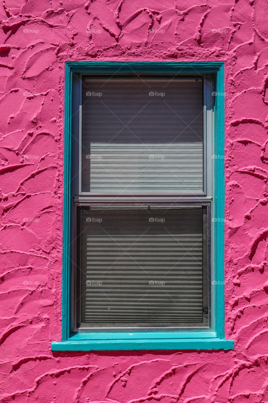 Close up view of a Mediterranean style stucco building, hot pink with a window with turquoise trim 