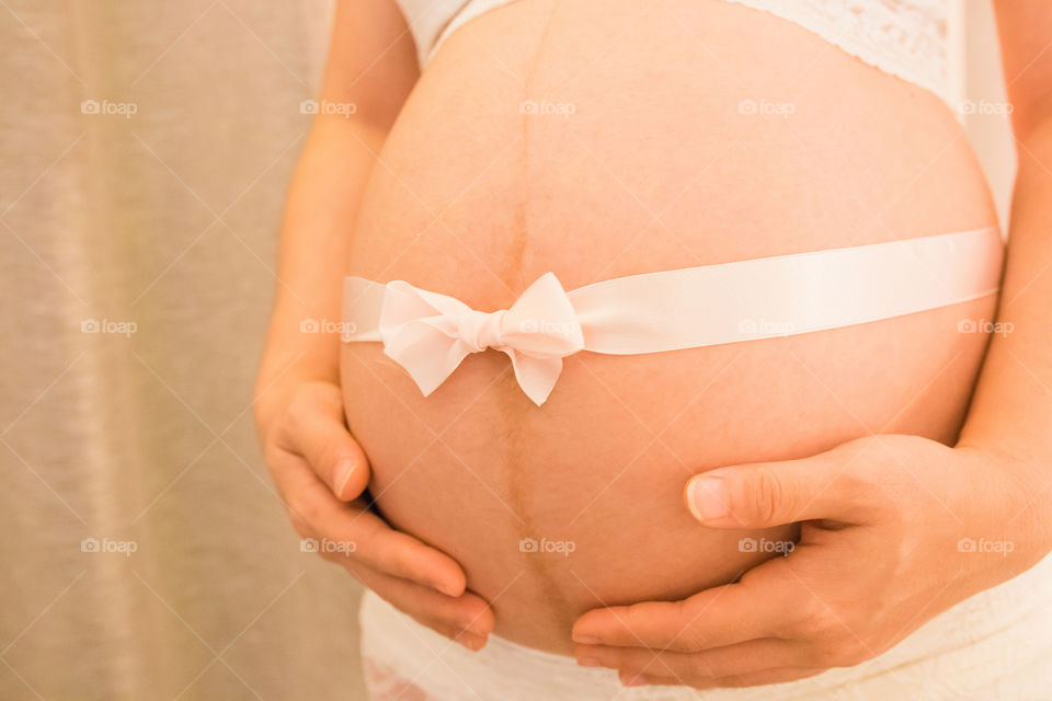 
Close up image of pregnant woman tummy with pink ribbon 

