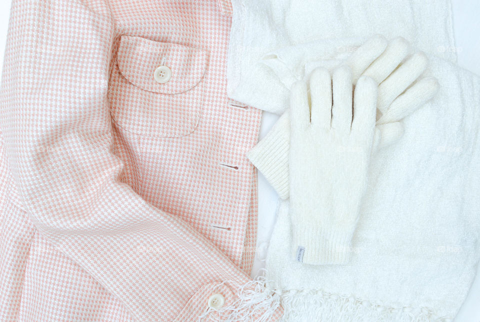 Flat lay of a coat with a white scarf and gloves