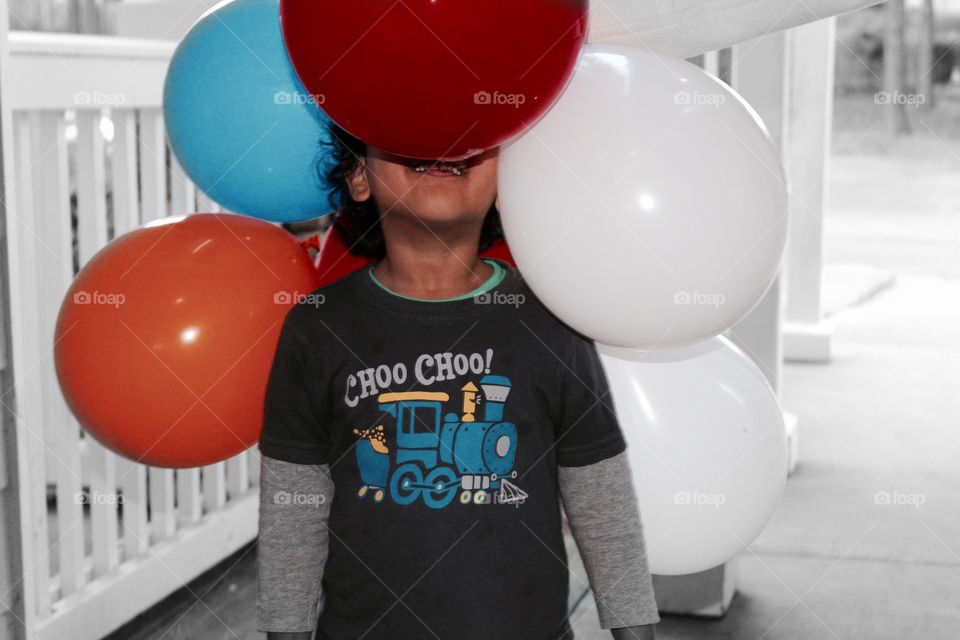 Happy kid hiding face in balloons 