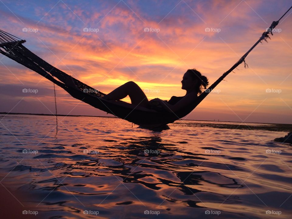 Silhouette of woman in hammock at sunset on the beach