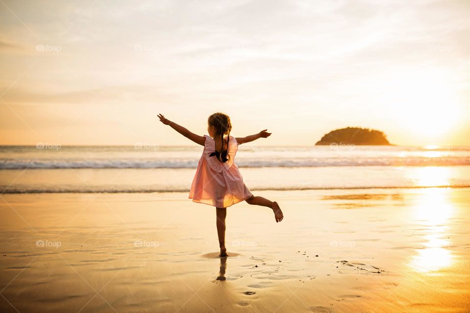 Little girl having fun on sandy beach on sunset 