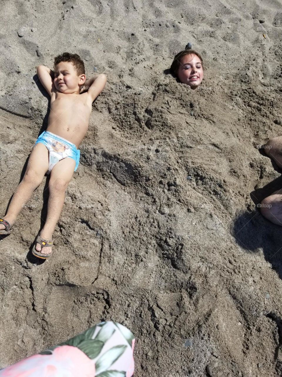 Beach summertime fun a kid buried and a kid tanning 