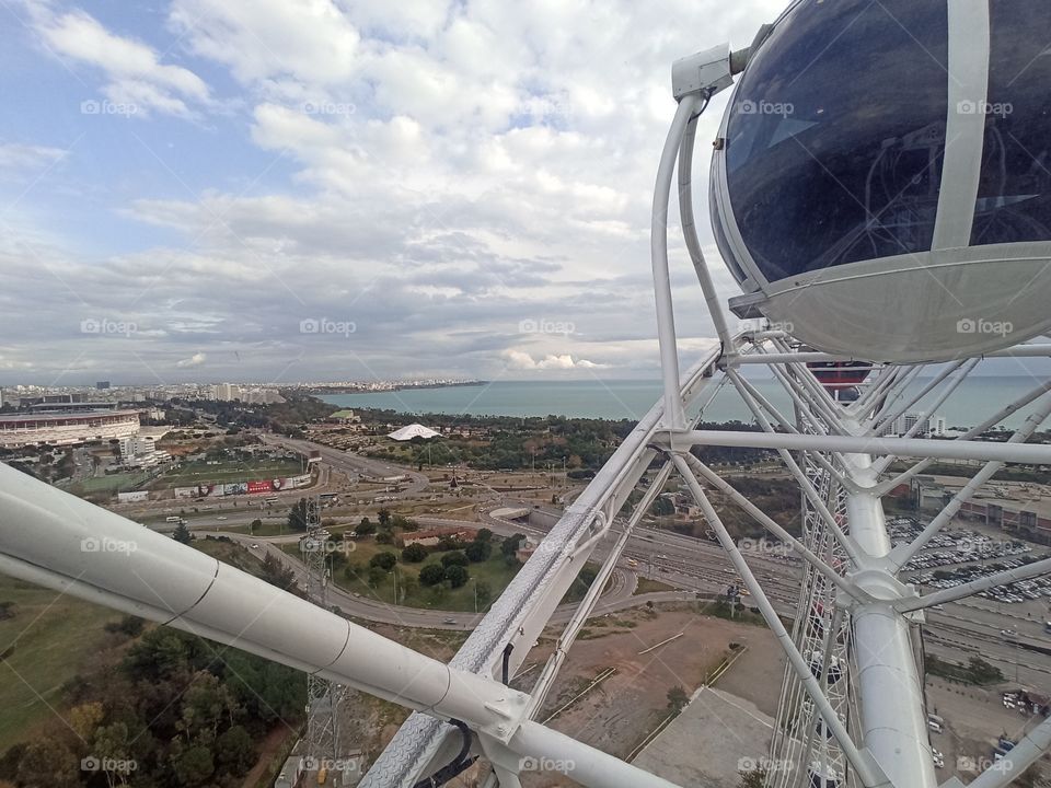 A photo of cityscape, landscape, seascape and cloudy sky from the cabin of ferris wheel