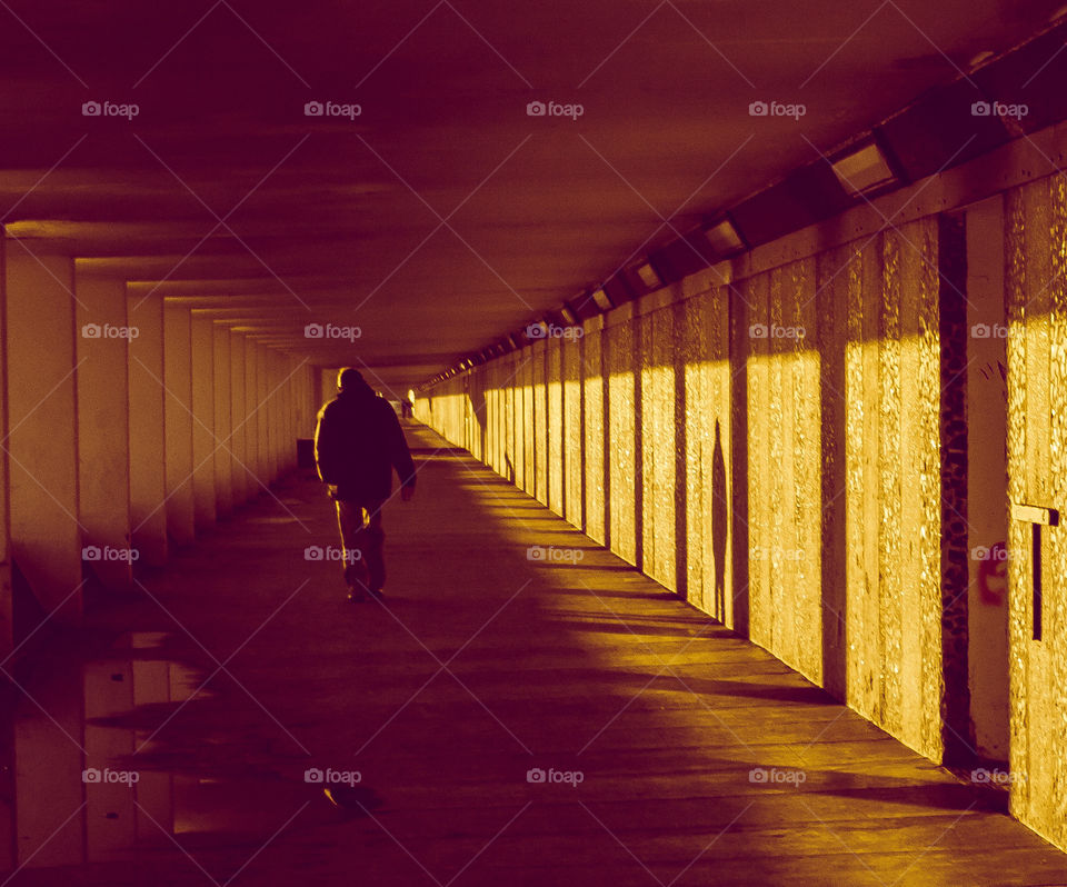 Long shadows are cast along an underground walkway, one man walking can be seen in the distance, in vibrant sunset colours