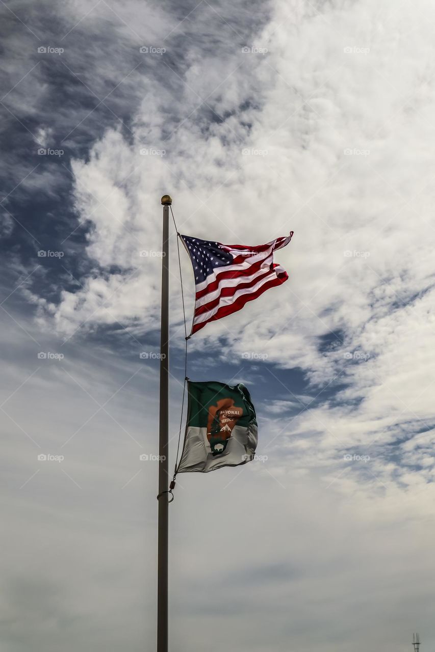 American flag flying proudly in the sky along with national parks flag with a dramatic cloudy sky in the background 