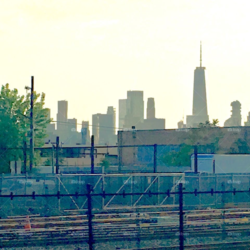 A view across the train tracks by Borden Avenue in Long Island City, Queens, NY onto the Manhattan skyline in the distance. The sun is about to set and lights up the sky in a faint hint of gold. Photo from 2020. Hypnotic Productions
