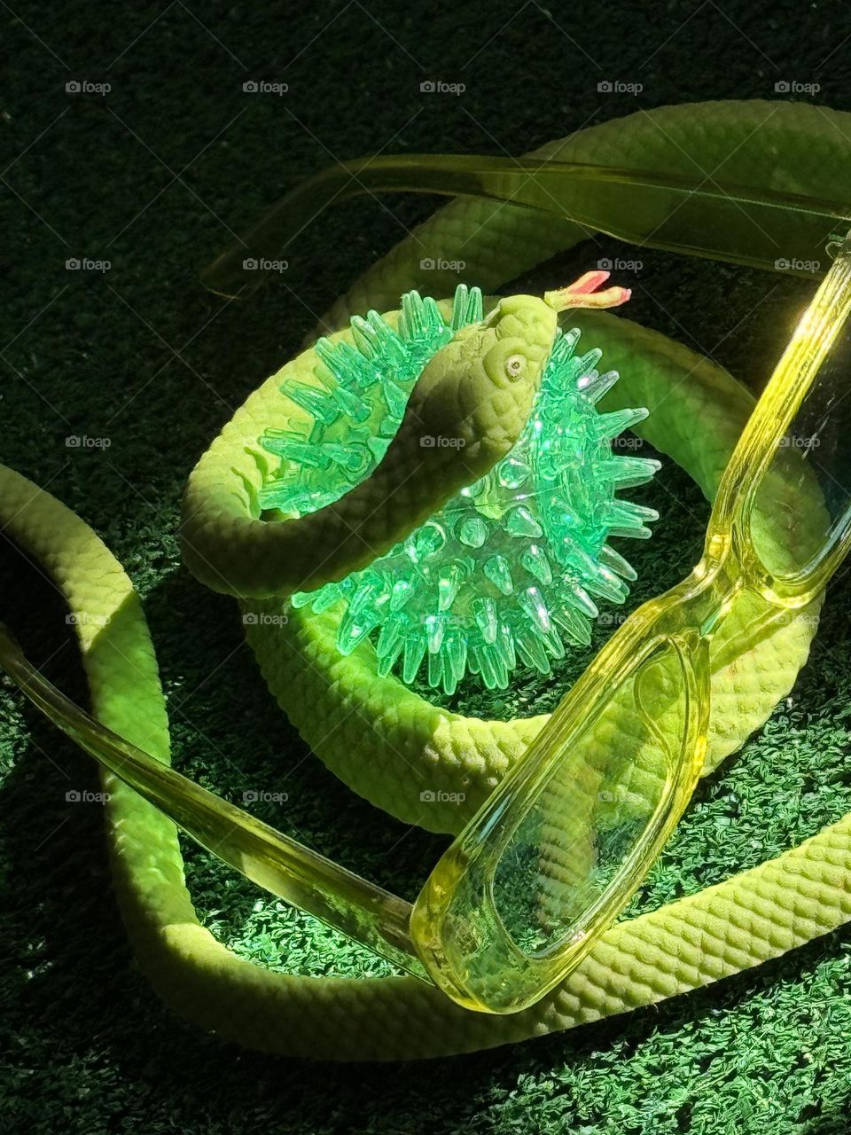 Rubber green snake on fake grass with lime colored eyeglasses and a spiky green light-up toy ball
