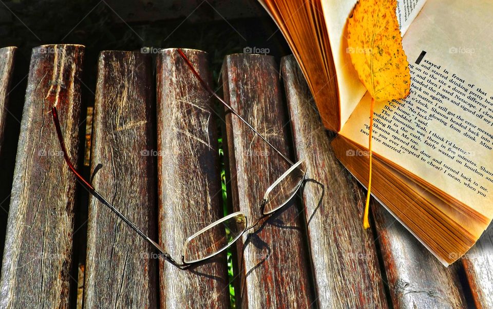 The open book with a yellow leaf and the glasses on the square bench