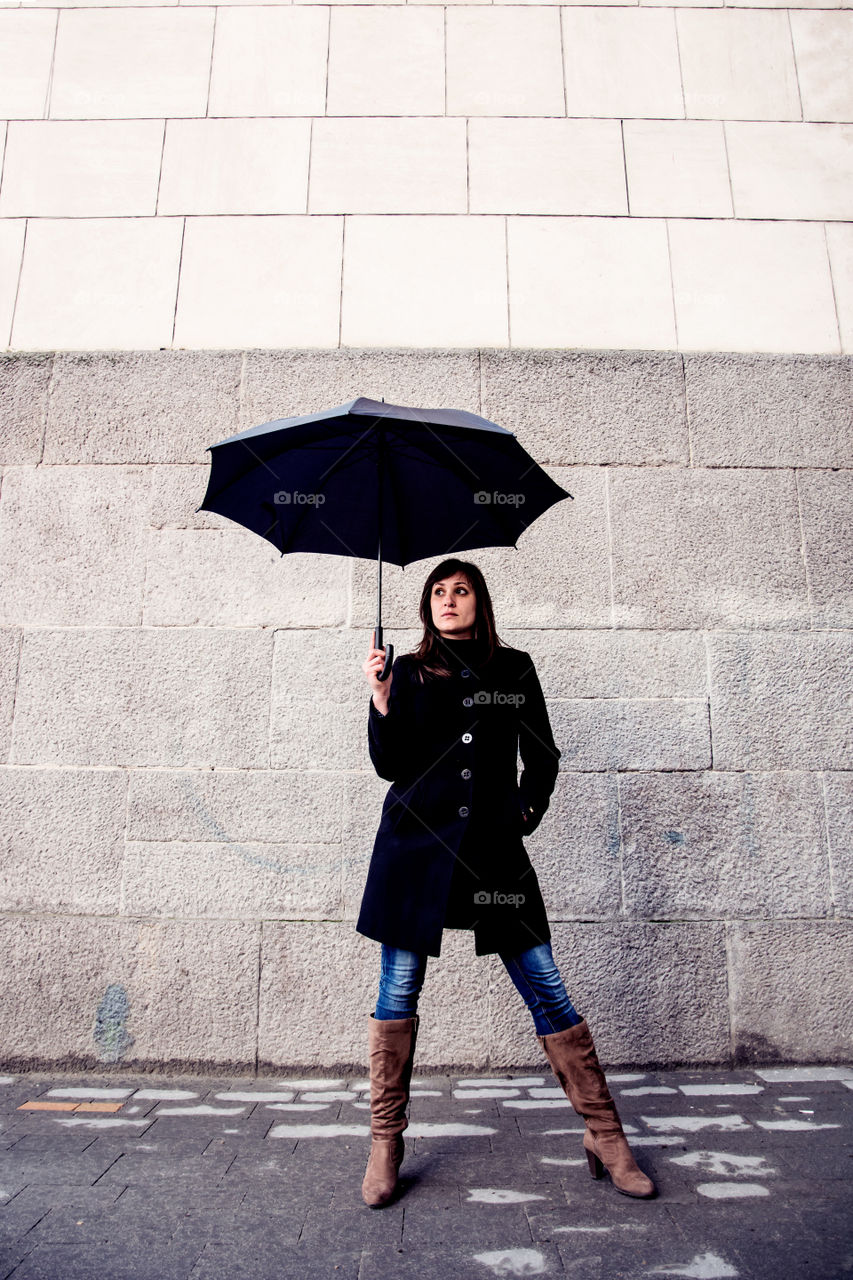 Young woman holding umbrella in front of wall