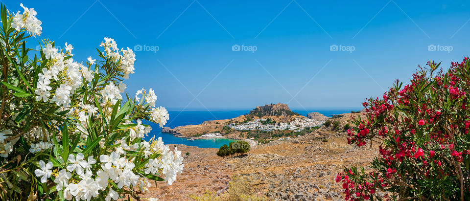 Panoramic distant view at remains of the ancient Lindos Acropolis BC300 and medieval castle build on top of it on a clifftop rock. Below is beautiful whitewashed small Lindos town. Lindos. Island of Rhodes. Greece . Europe.