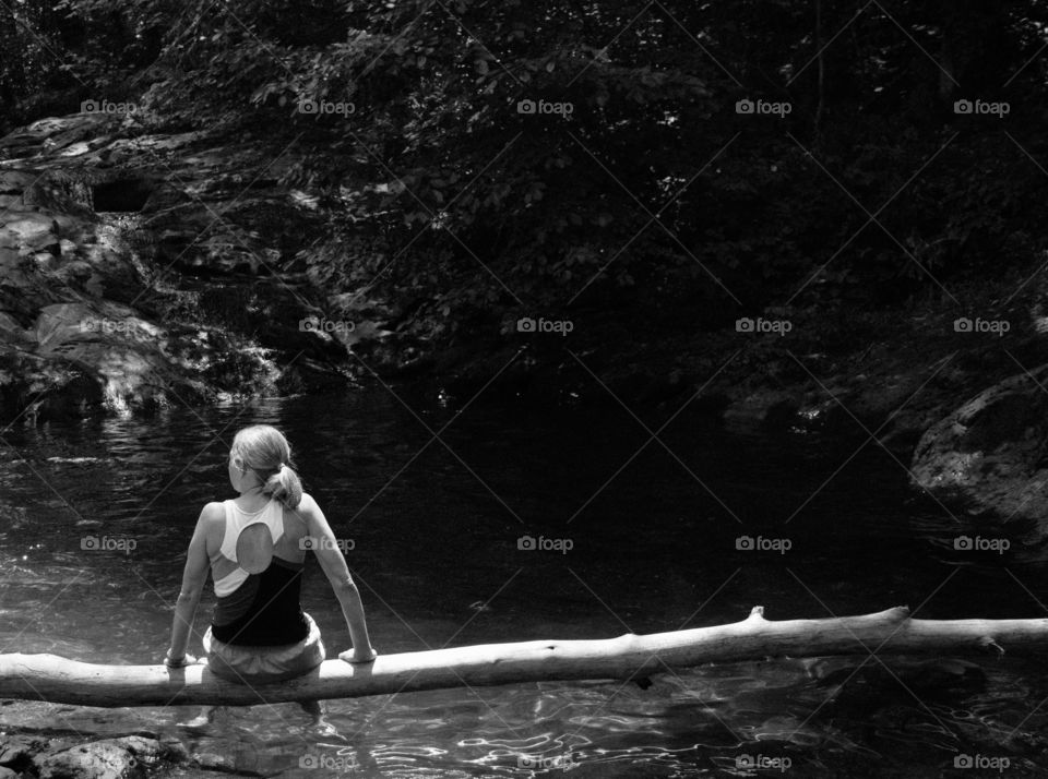 Woman Sits on Log by a Natural Pool