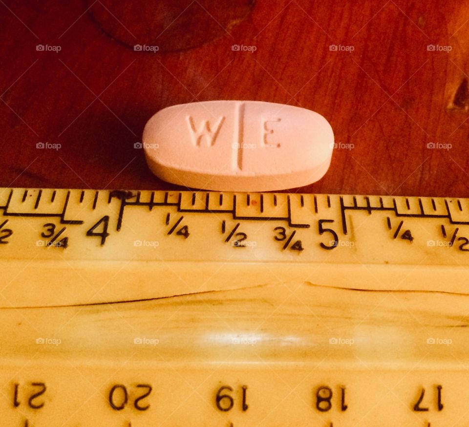 Large pink pill against plastic yellow ruler