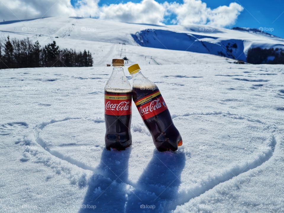 two bottles of Coca Cola resting on the snow in the mountains