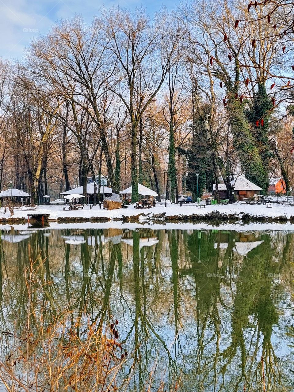 Winter landscape by the lake.  Coast covered with snow,  a beautiful sunny day with the reflection of the trees on the surface of the water