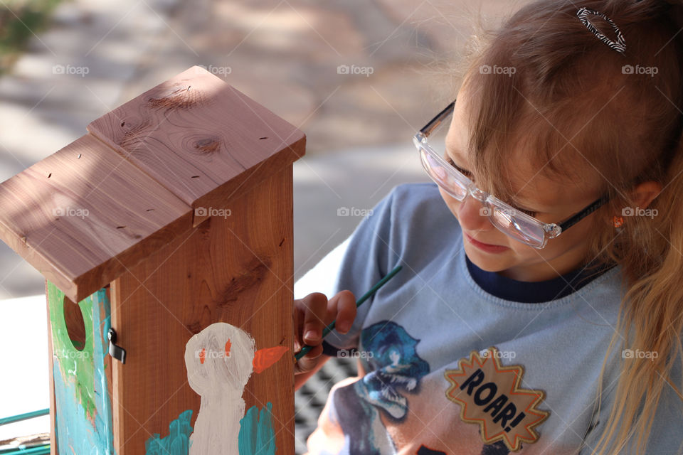 Child painting a wooden bird house