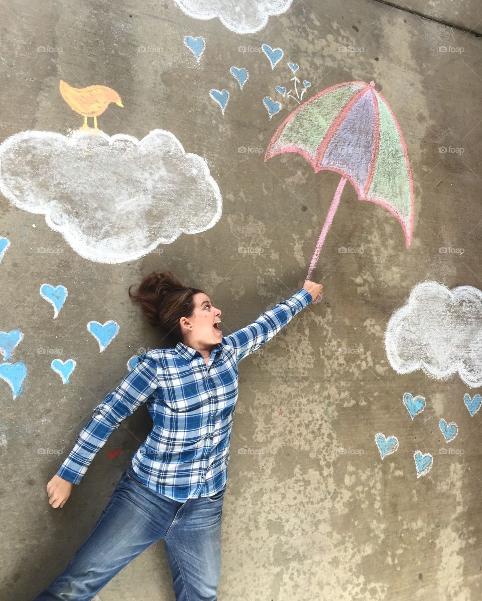 Woman lying on street holding umbrella made up of chalk