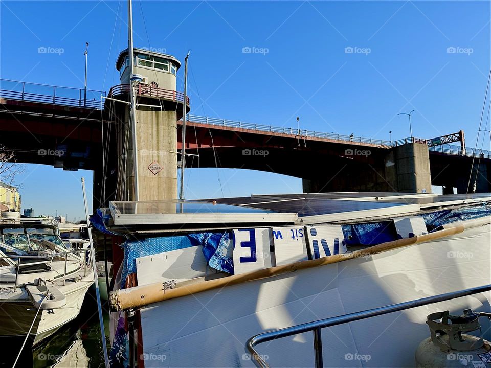This is the “Pulaski Bridge” at “Newtown Creek” in LIC, Queens seen from our “28 foot 1969 Luhrs” cabin cruiser, the boat that is our home. There is a gutter to collect rain water and solar panels harness the sun’s energy. 2023. Hypnotic Productions