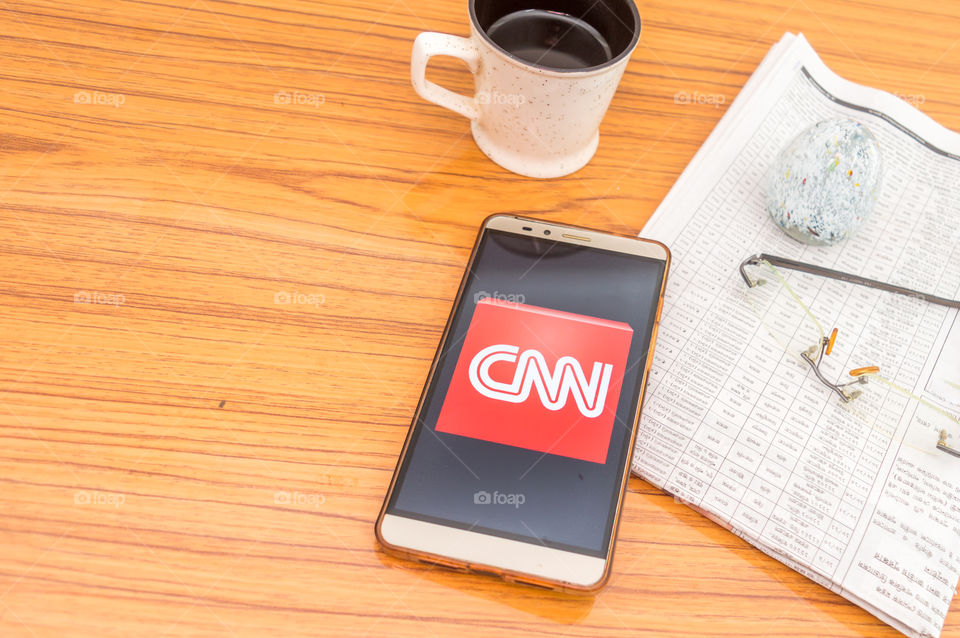 Kolkata, India, February 3, 2019: CNN news app (application) visible on mobile phone screen beautifully placed over a wooden table with a newspaper and a cup of coffee. A Technology Product Shoot.
