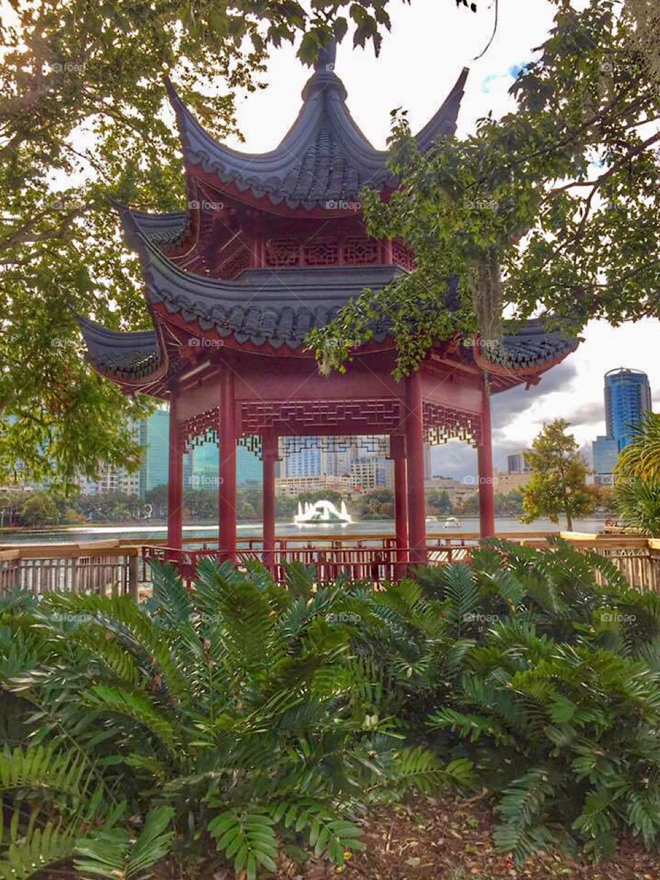 The red Chinese ting pagoda pavilion at Lake Eola Park in downtown Orlando, Florida with the Lake Eola fountain in the background 