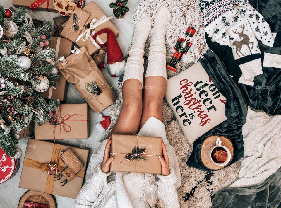 Top view of a woman holding a brown gift box on a carpet beside a Christmas tree