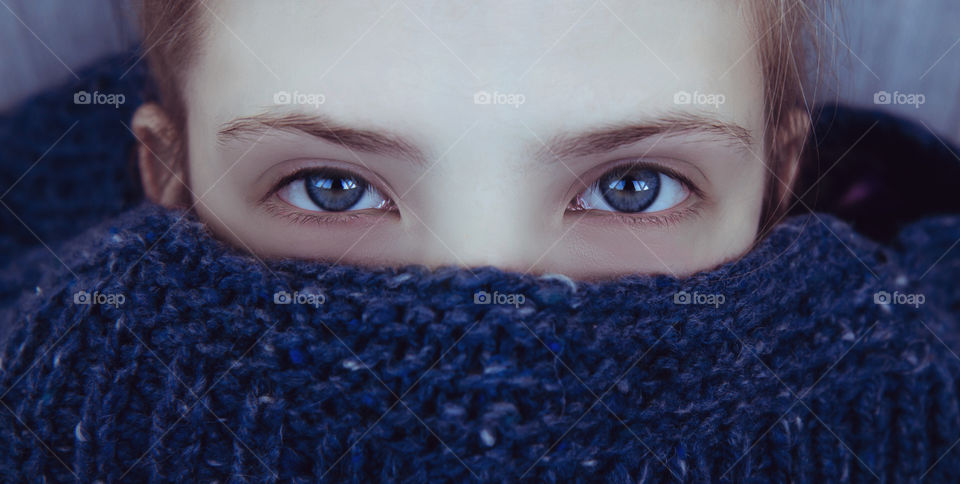 Beautiful girl with blue eyes wrapped herself in a warm blue knitted sweater