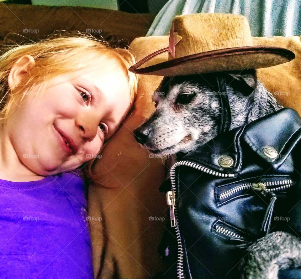 Girl adoring a Chihuahua dog wearing his cowboy hat and black leather cowboy coat.