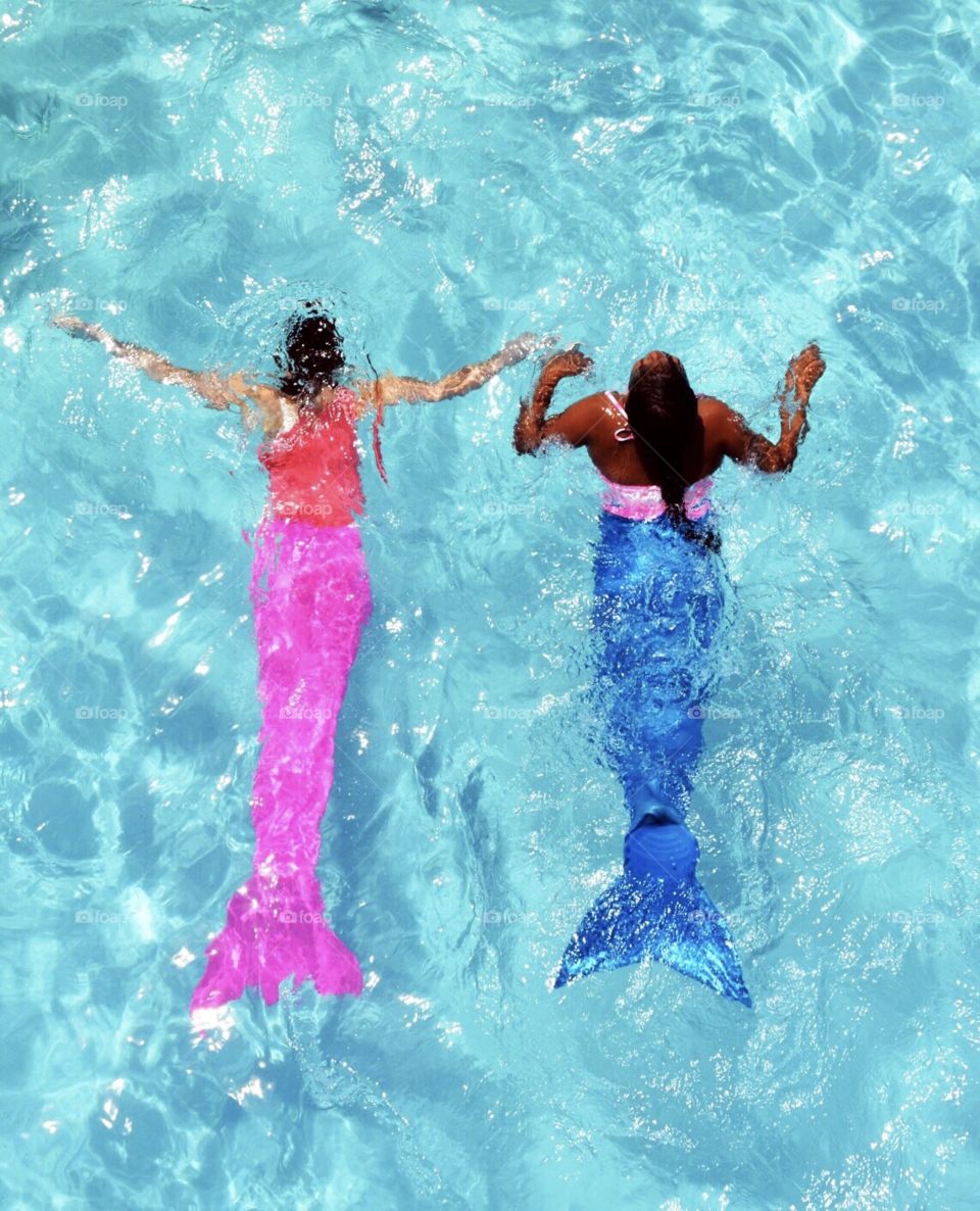 Two young girls swimming in a pool with mermaid tails. 