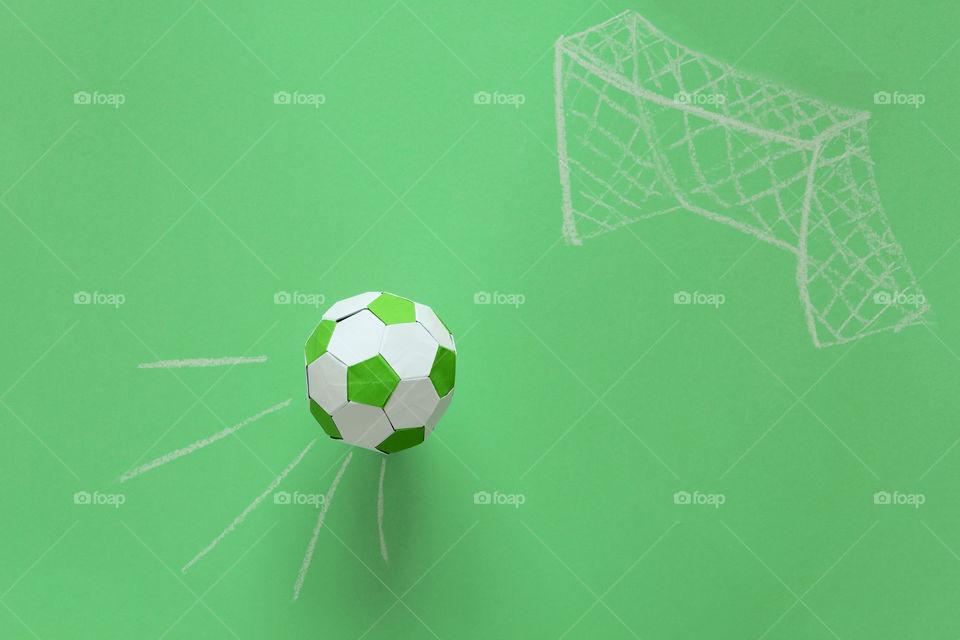 Paper soccer ball flying into goal painted by chalk on green background. Origami. Paper craft. Soccer game concept.