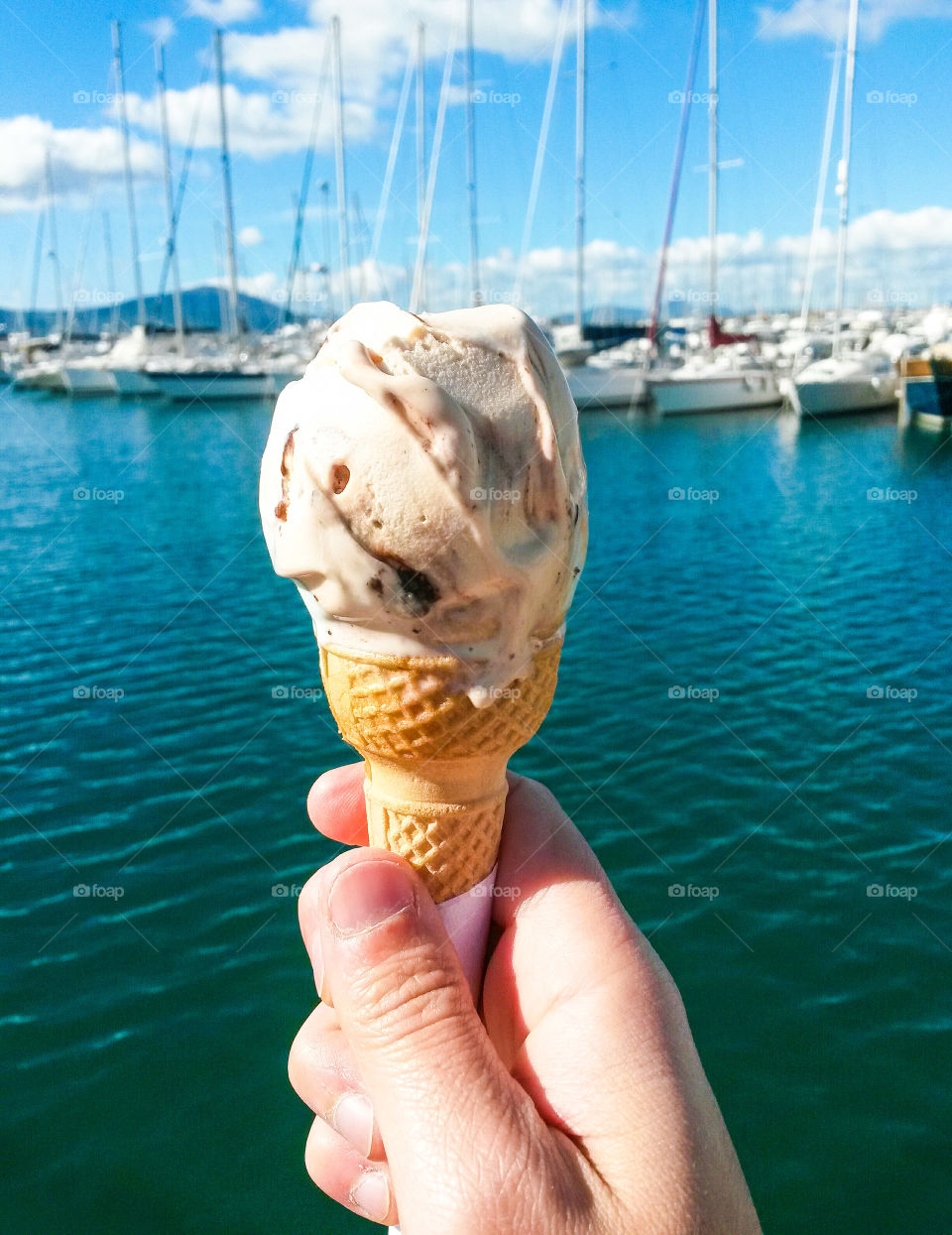 Person holding ice cream cone in hand at sea side