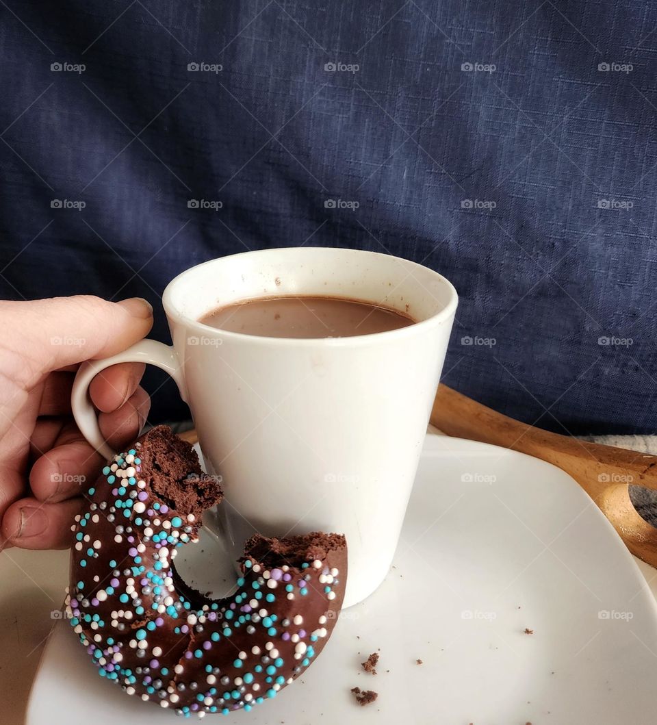 Enjoying a cup of coffee and a homemade chocolate donut with sprinkles.