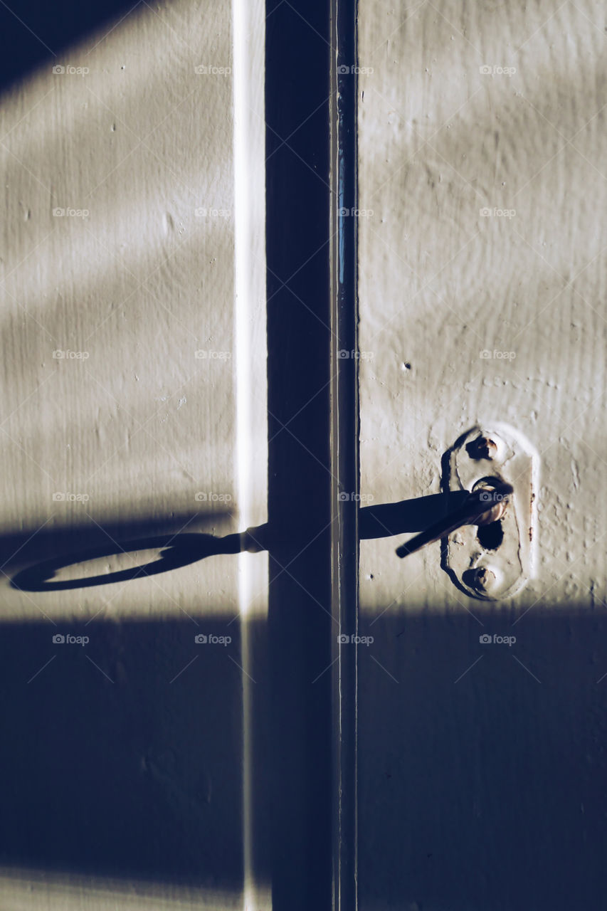 The sun hits the old wooden door and the key in the lock making long shadows on the white paint 