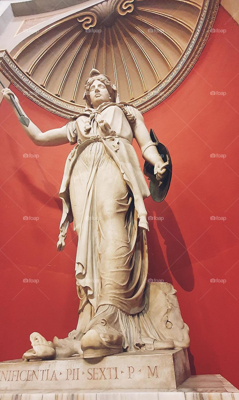This is a classical statue from Rome, featuring intricate details and a Latin inscription on its base, likely displayed in a museum or historic site.