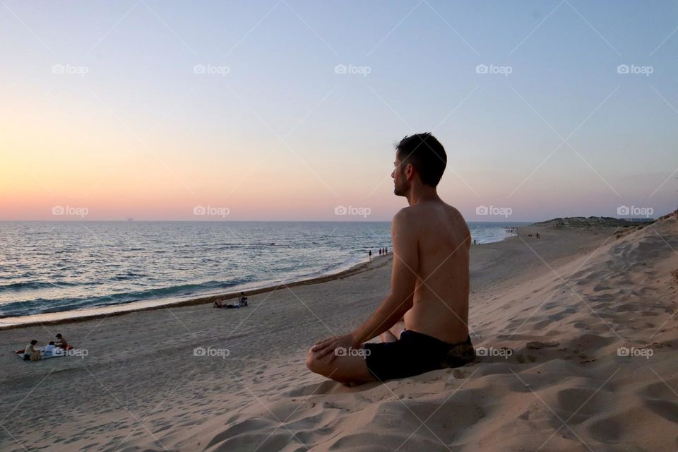 Man meditate on the sand dune In front of the sea during sunset