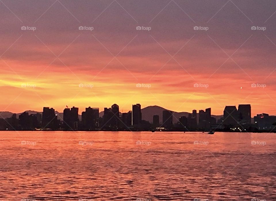 Sunrise over San Diego bay with city skyline outlined by fiery light. 