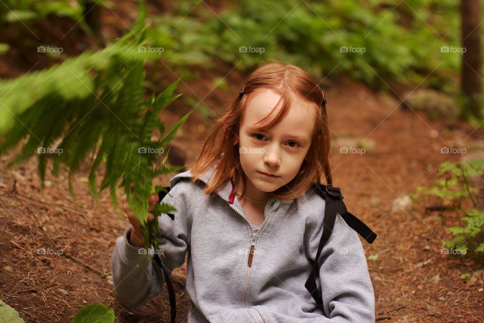 Little girl in the mountains holds a fern leaf in her hands