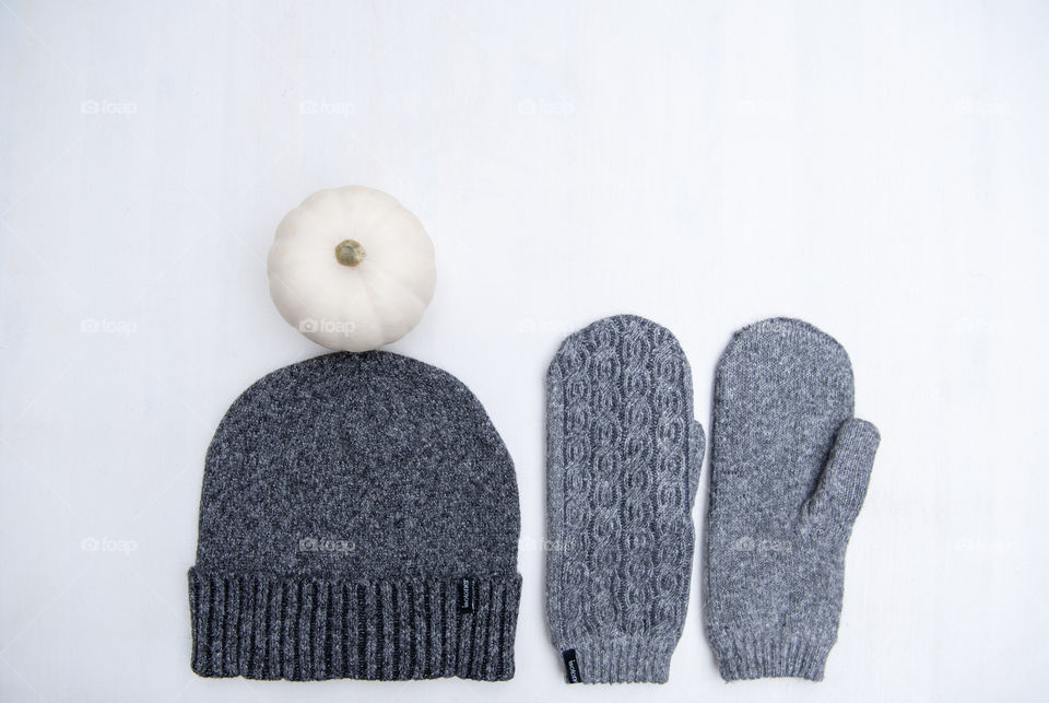 Flat lay of a pair of mittens and a beanie hat topped with a white pumpkin