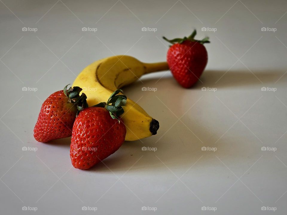 A banana and some strawberries placed on a table with a white background.