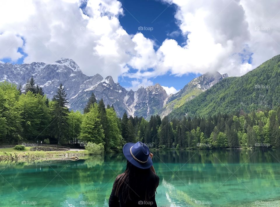 Woman from behind looking at amazing view of lake and mountains with beautiful sky clouds 