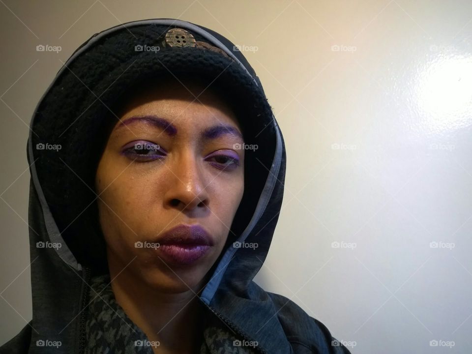 Woman wearing a hat and a hoodie, while leaning against a wall.