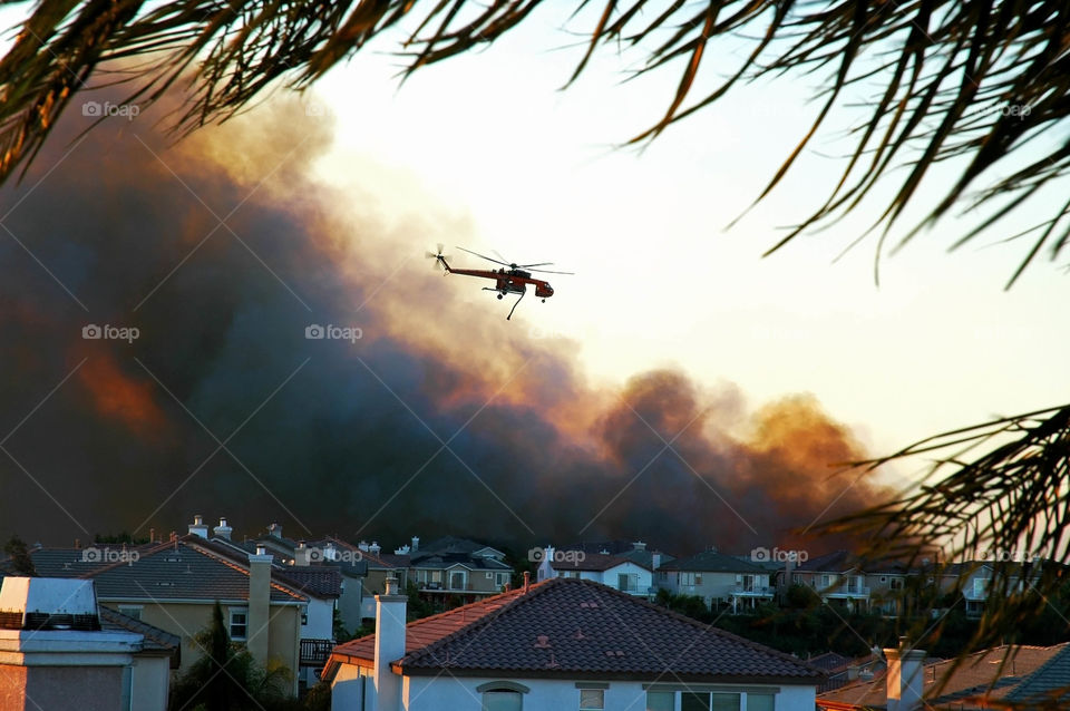 A water dropping helicopter attempts to put out a California wildfire threatening a housing development.