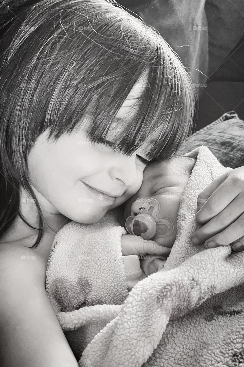 A young boy greets his newborn sister for the first time, holding her gently and smiling with joy