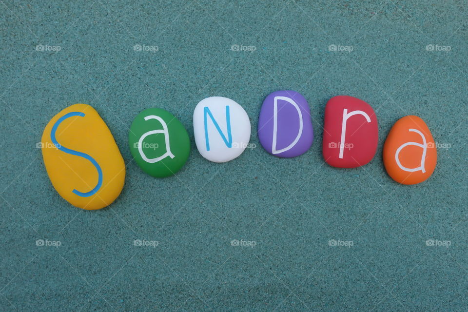 Sandra, feminine given name composed with colores stones over green sand 