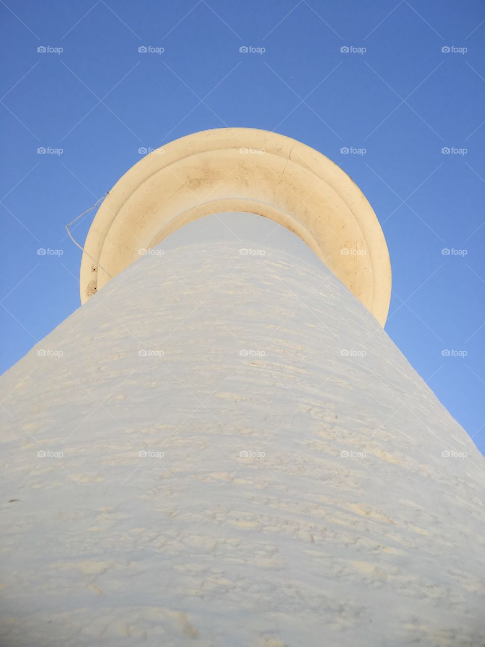 White lighthouse against vivid blue sky, ground up perspective minimalist, clean