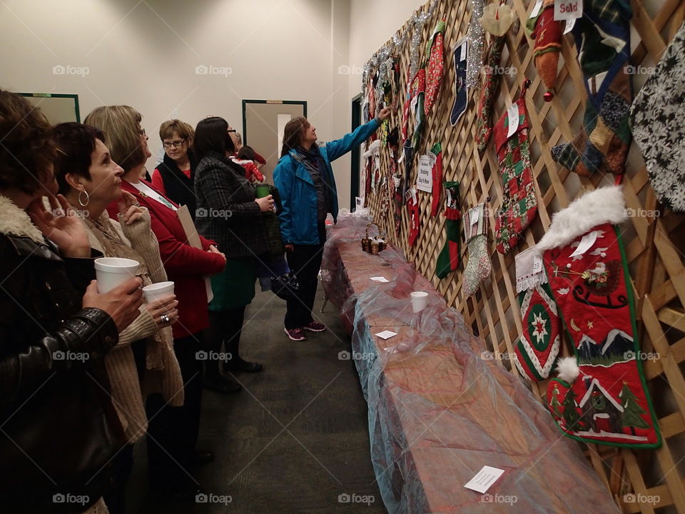 A crowd gathers at a holiday bazaar to view Christmas ornaments hanging on a wall. 