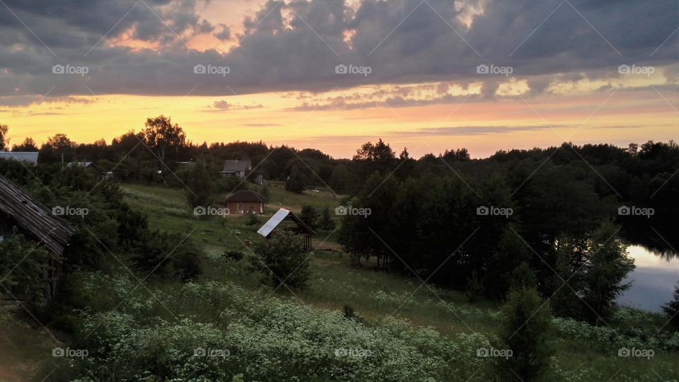 A bright sunset over a small village immersed  in summer greenery.