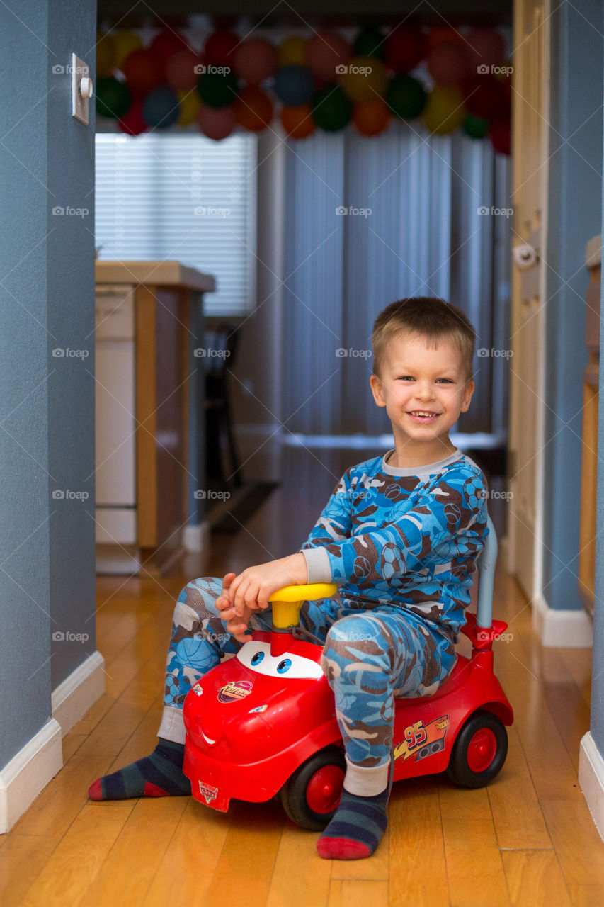 Toddler in pajamas on red toy car inside the house