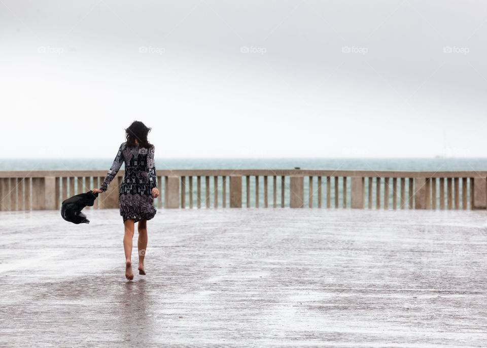 woman in barefoot walks under the rain on promenade